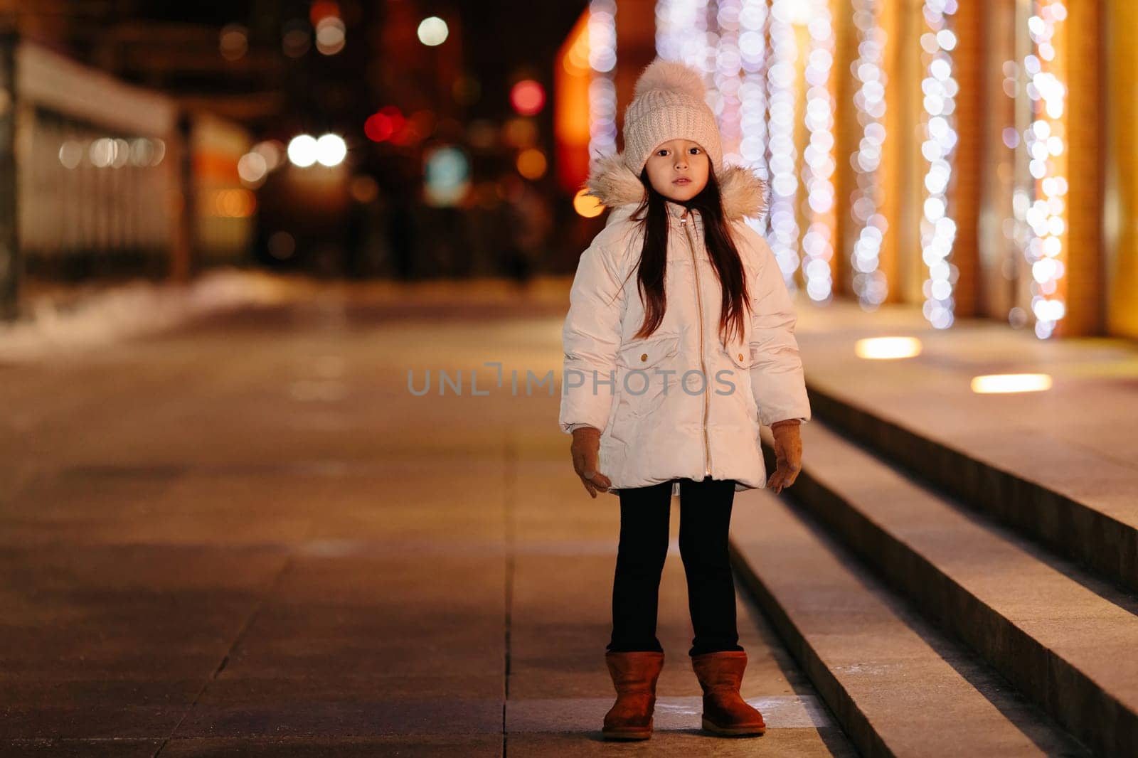 Cute happy little girl walks on the streets of a big city in the evening in winter. Christmas holidays.
