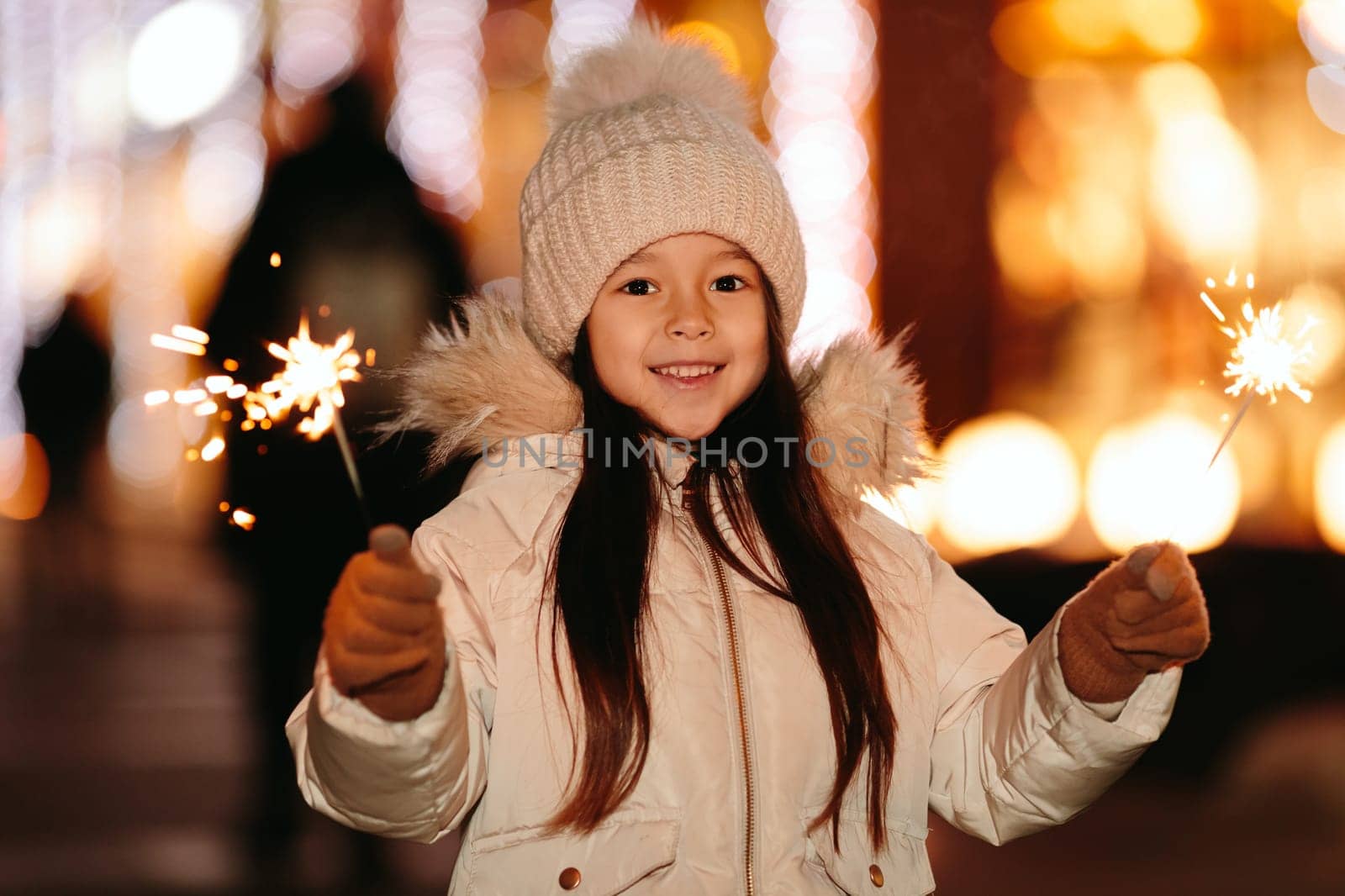 Cute smiling little girl with bengal lights on the street in the evening in winter. Christmas holidays