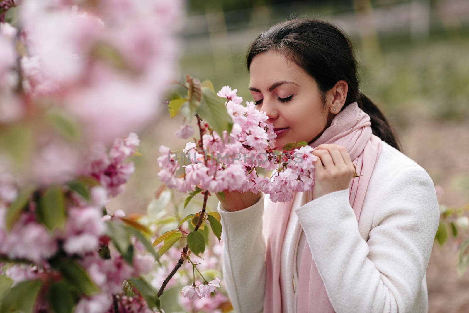 Beautiful young brunette woman enjoying spring day in park during Sakura cherry blossom season