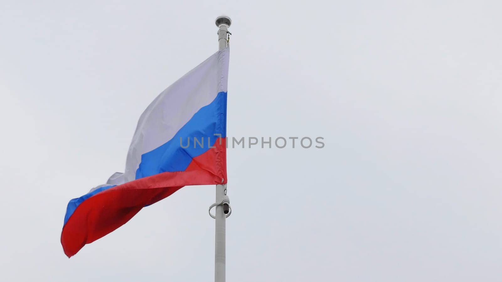 Russian flag on the flagpole waving in the wind against a blue sky with clouds.