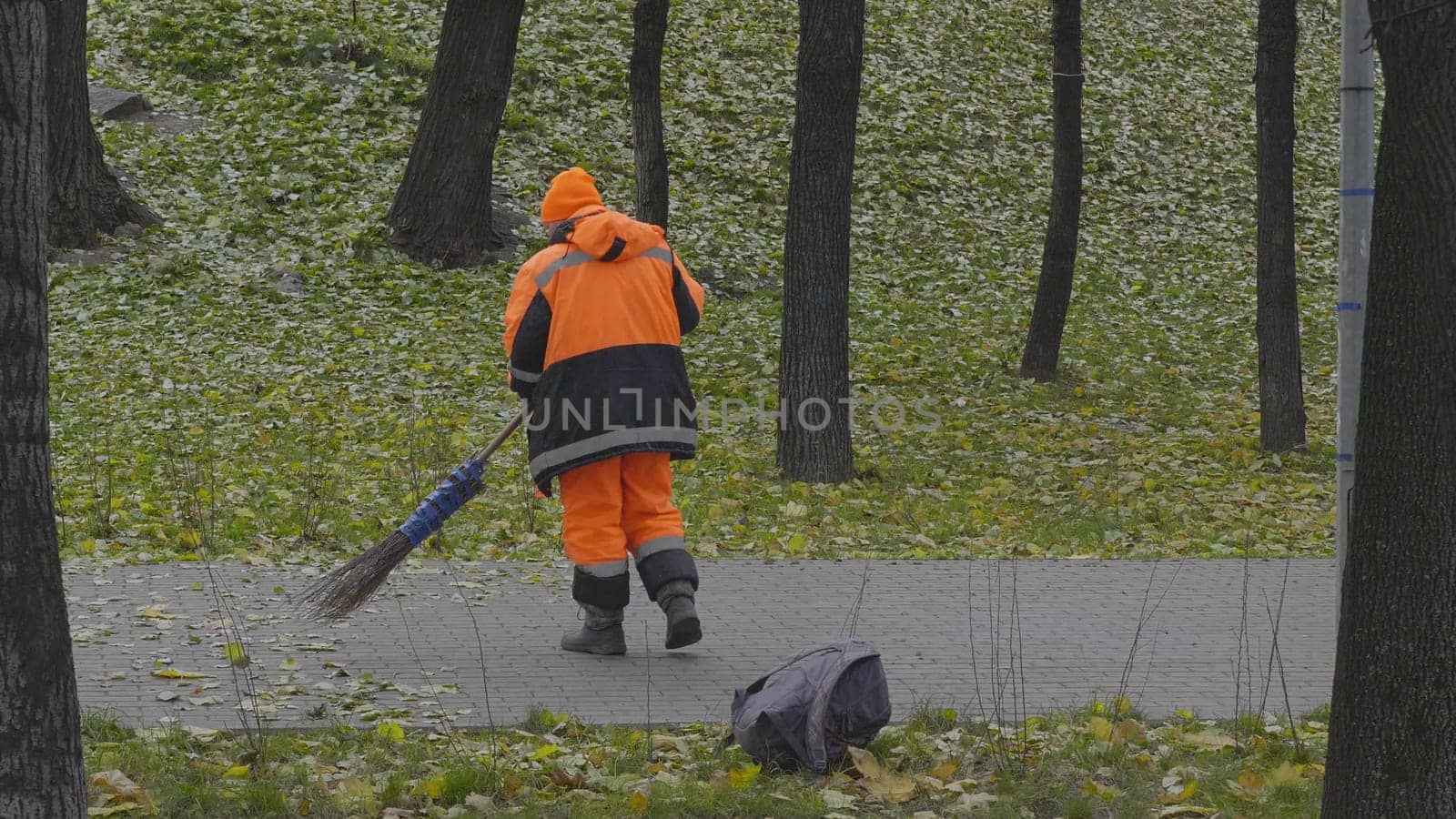 Worker sweeps autumn leaves with a broom from the sidewalk.