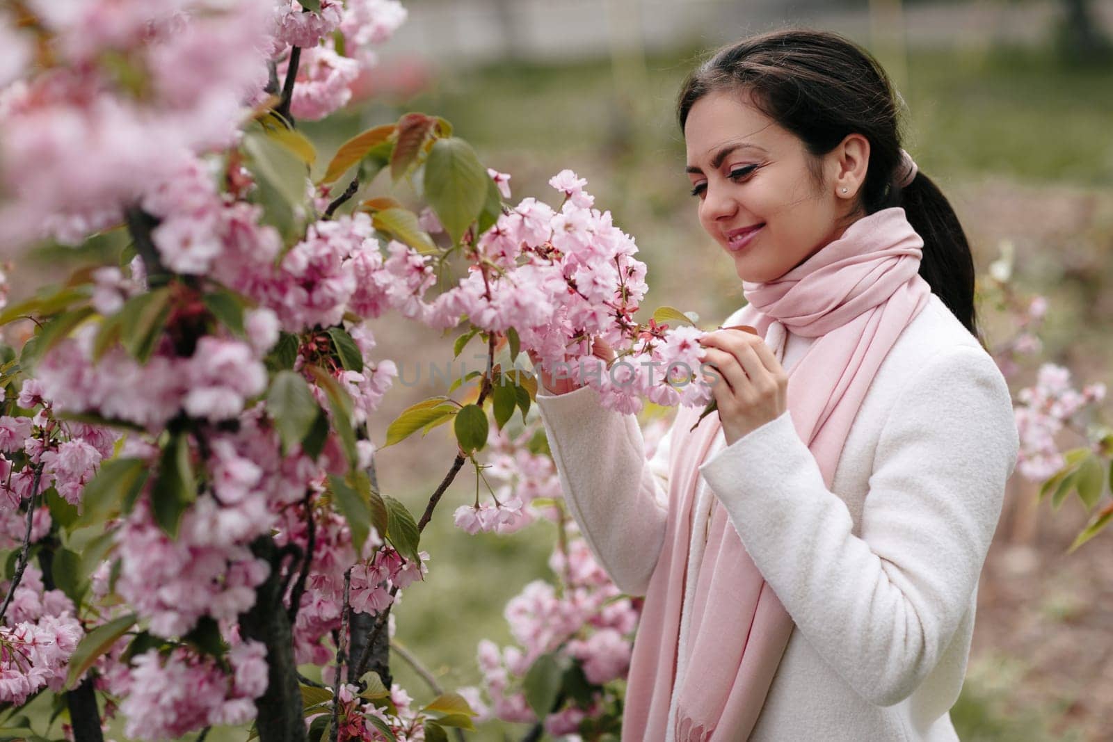 Beautiful young brunette woman enjoying spring day in park during Sakura cherry blossom season