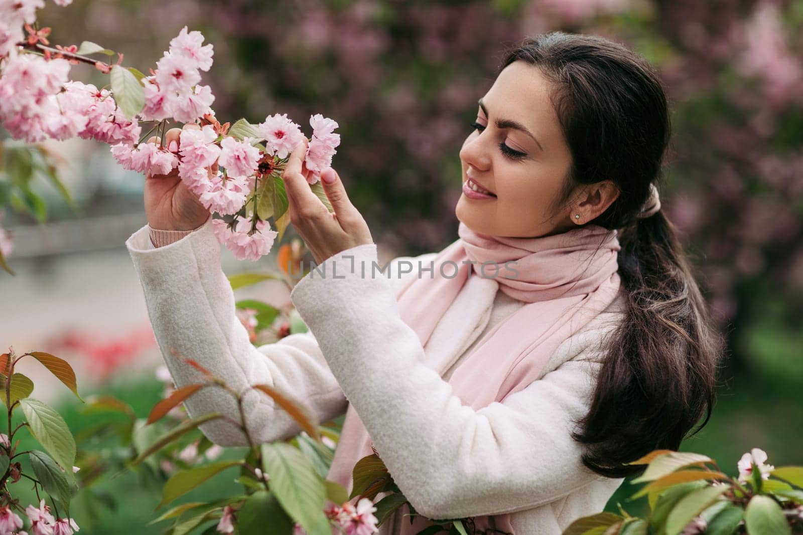 Beautiful young brunette woman enjoying spring day in park during Sakura cherry blossom season