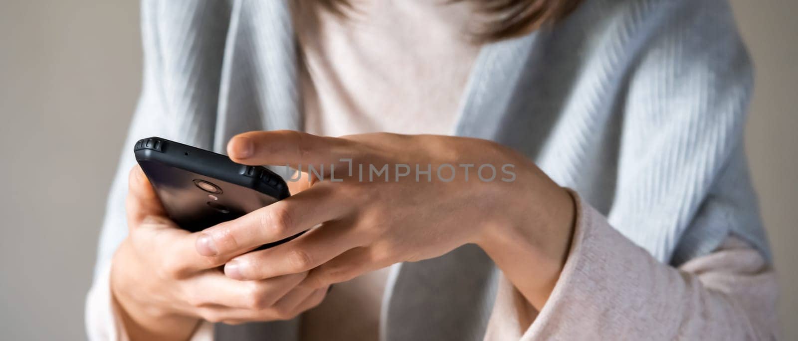 A young well-groomed woman holds a smartphone in her hands, communicates with colleagues, friends, a girl in a casual sweater works online using her mobile device.