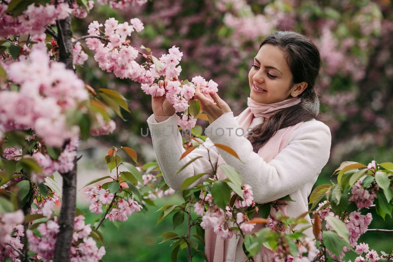 Beautiful young brunette woman enjoying spring day in park during Sakura cherry blossom season