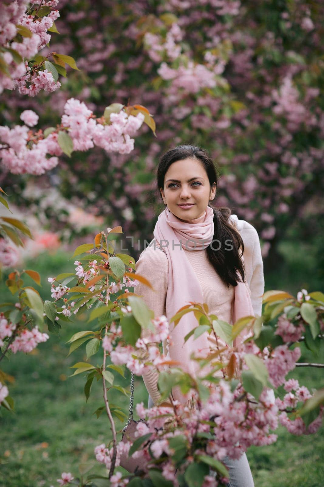 Beautiful young brunette woman enjoying spring day in park during Sakura cherry blossom season