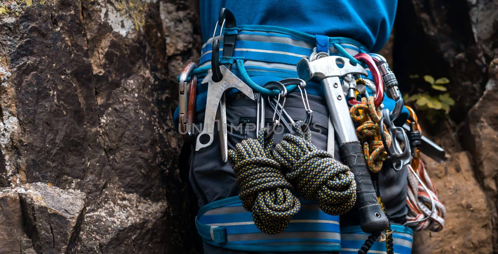 Climbing equipment, ropes, carabiners, harness, belay, hammer close-up of a rock-climber put on by a man, the traveler leads an active lifestyle and is engaged in mountaineering.