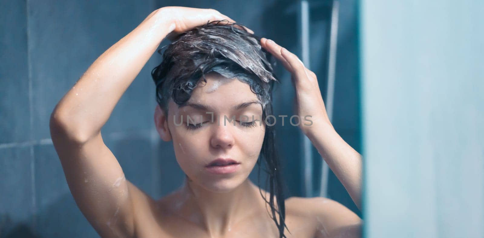 A young smiling girl takes a shower, washes with shampoo in a modern shower cabin, a woman relaxes, taking bath procedures, takes care of the beauty and health of her body.