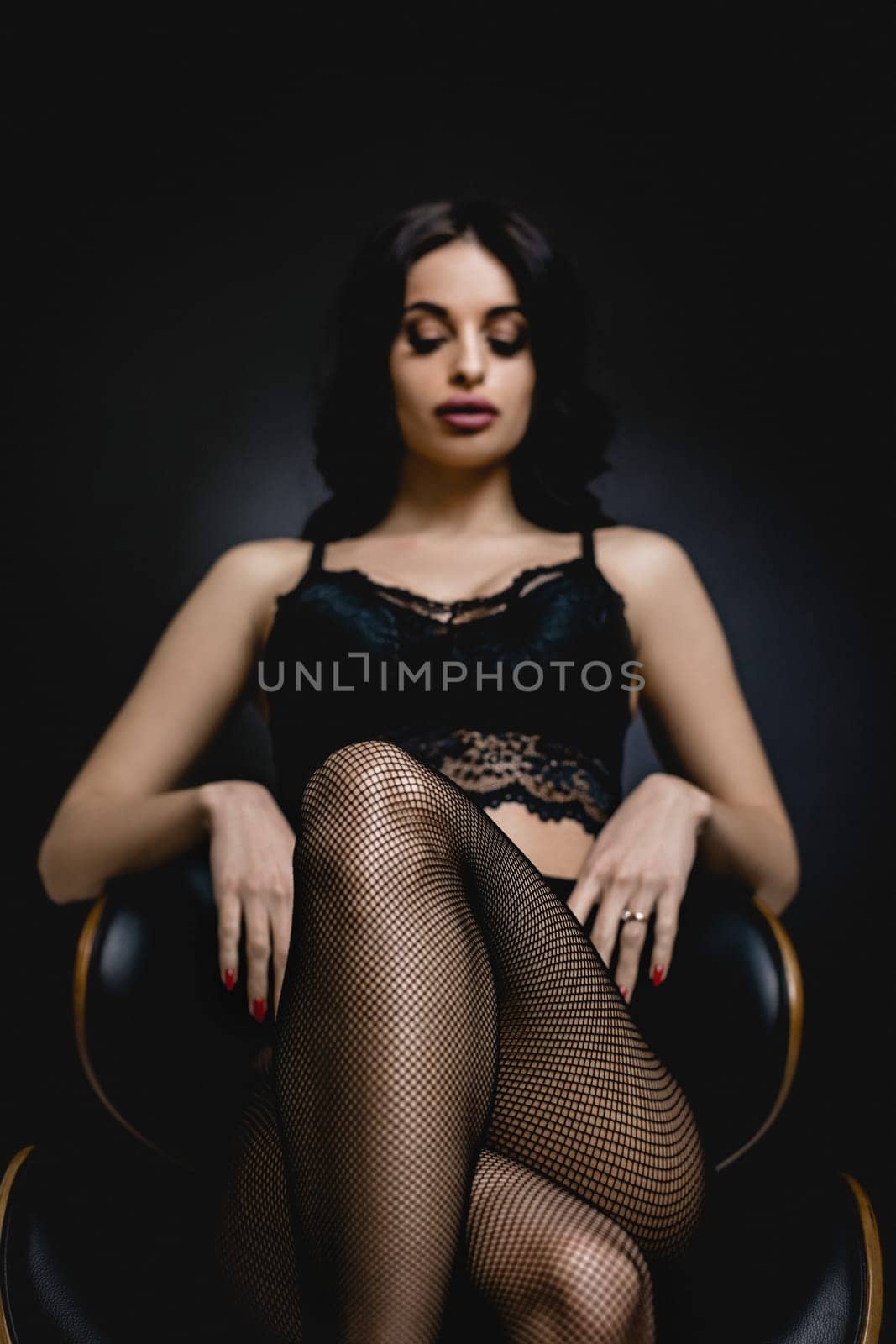 slim sexy woman in black stockings sits on a chair on a black background