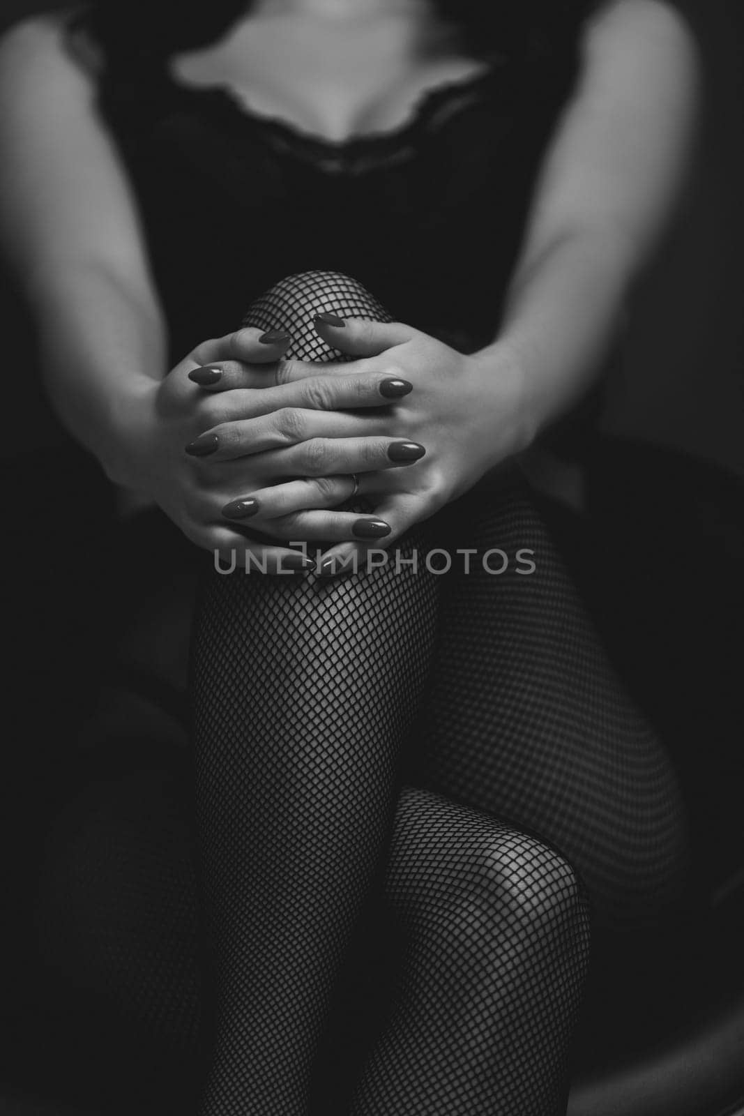 slim sexy woman in black stockings sits on a chair on a black background. black and white