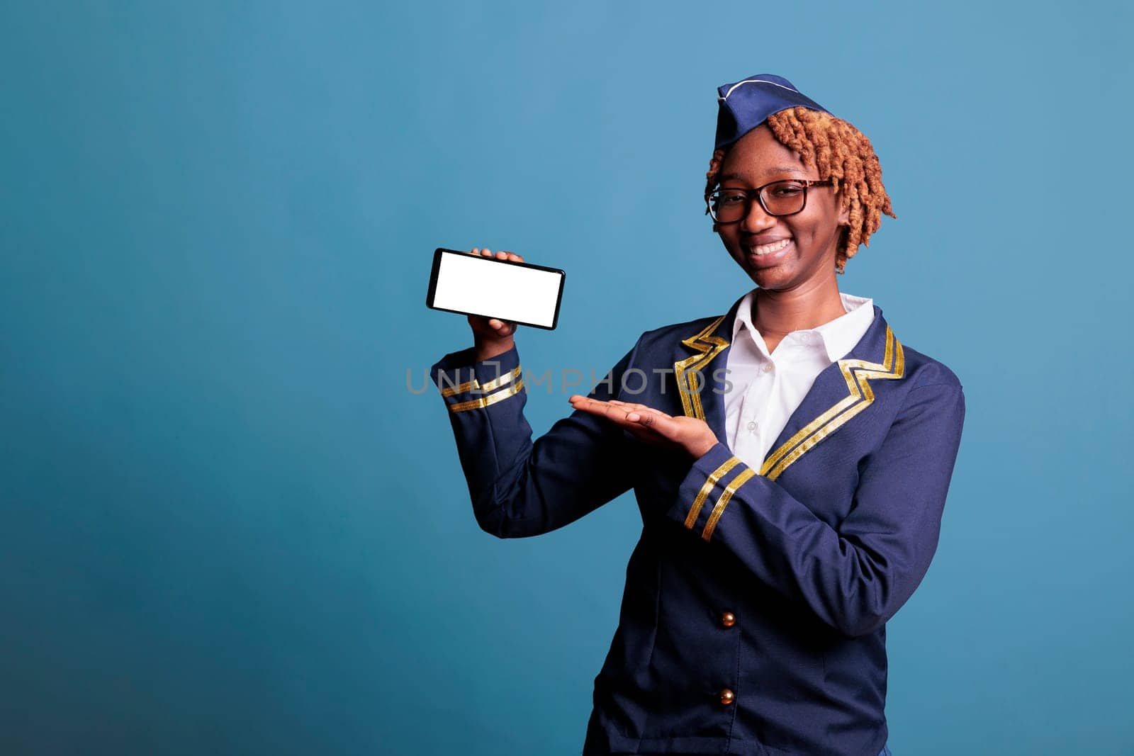 African american stewardess holding smartphone with white screen in a studio showing advertising space. Female flight attendant in uniform with cell phone with blank copy space.