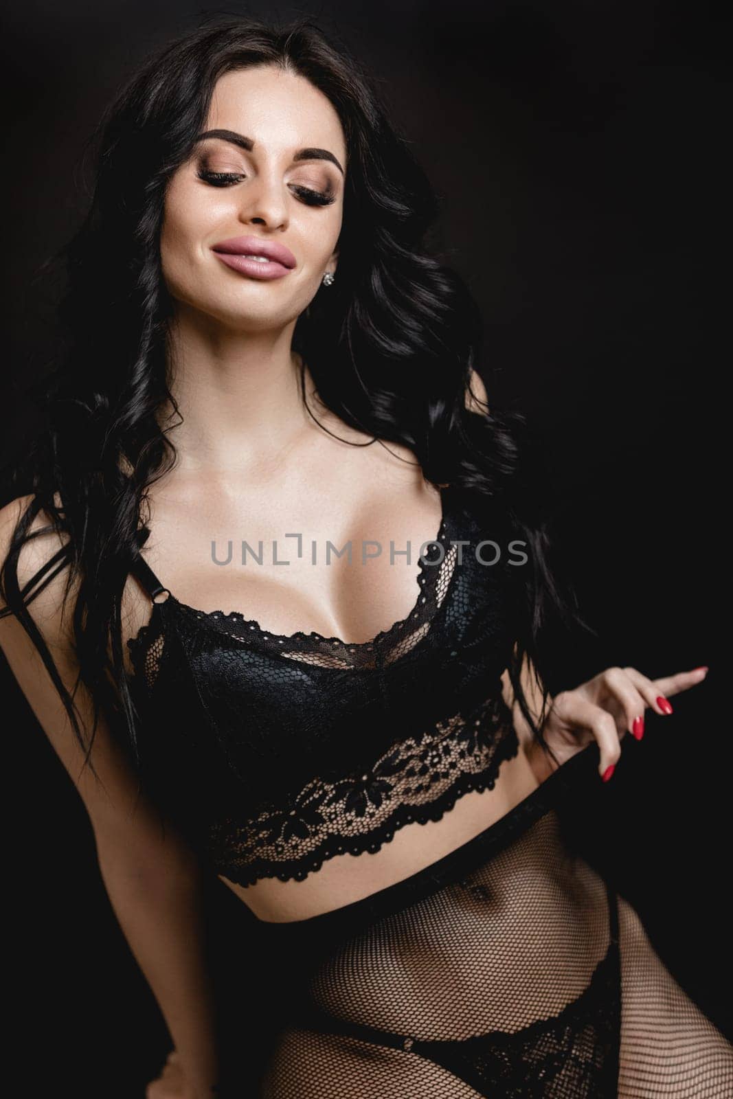 portrait of sexy woman in lace black sensual lingerie and pantyhose with long curly hair posing on black background in studio.