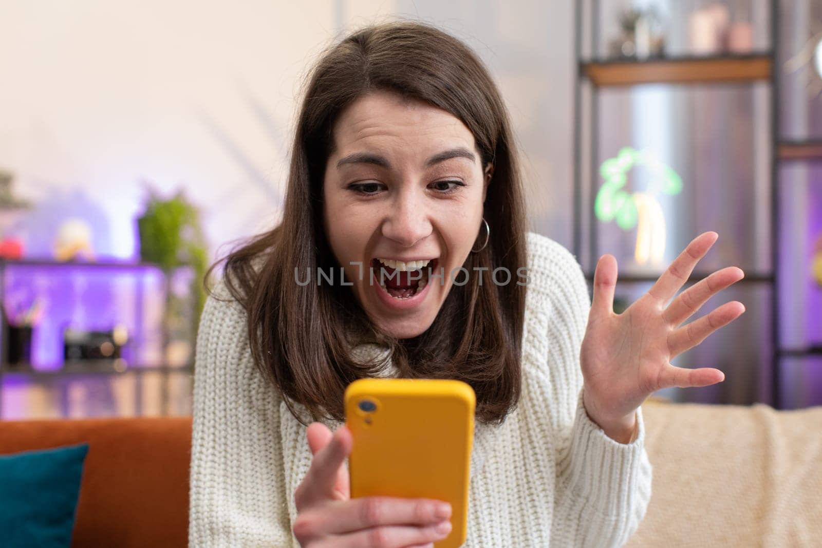 Oh my God Wow. Excited happy joyful winner young woman use smartphone typing browsing found out great win good news celebrate victory at home room apartment. Pretty girl with mobile phone on couch