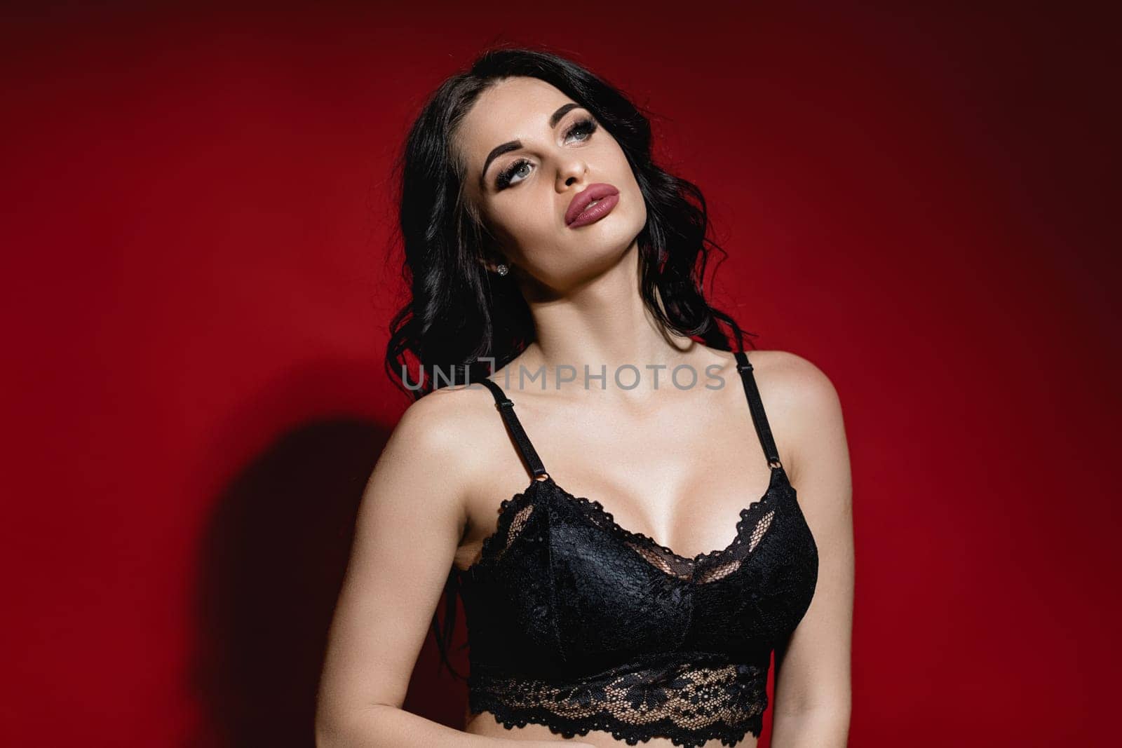 Sexy woman in lace black sensual lingerie with long curly hair posing on red background in studio.