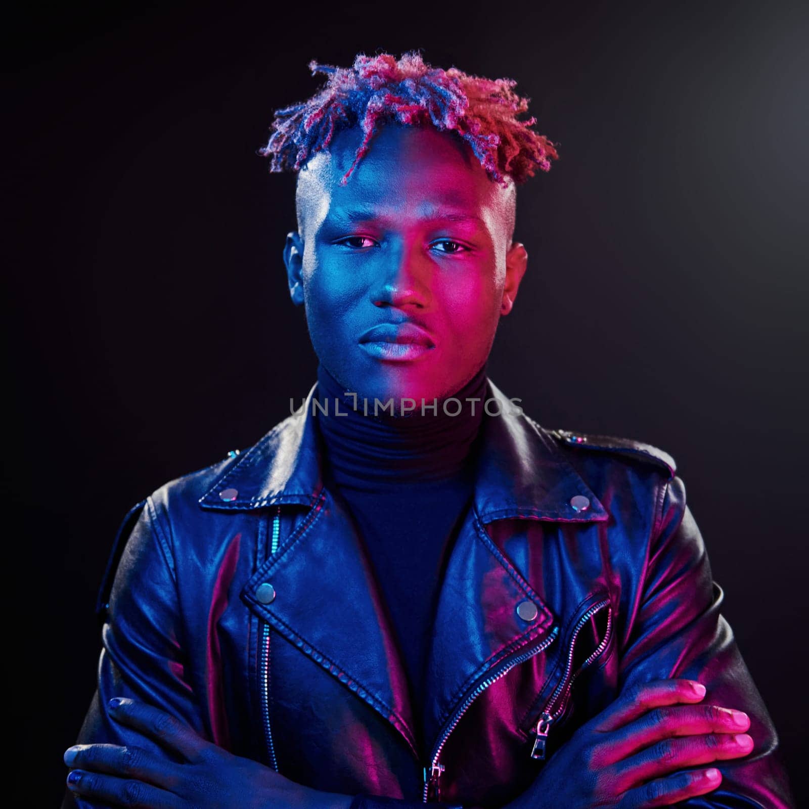 Futuristic neon lighting. Young african american man standing in studio with arms crossed.