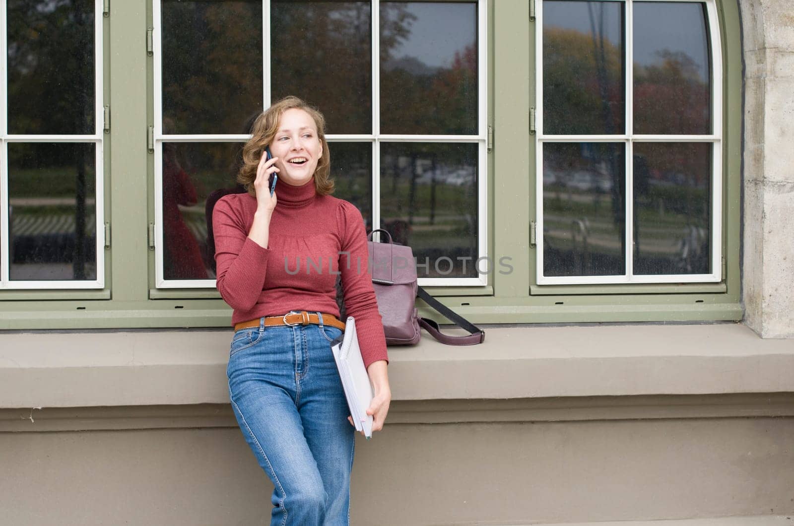 a young caucasian girl returns to college, stands with a backpack and notebooks and talks on the phone in a laugh, back to school, High quality photo