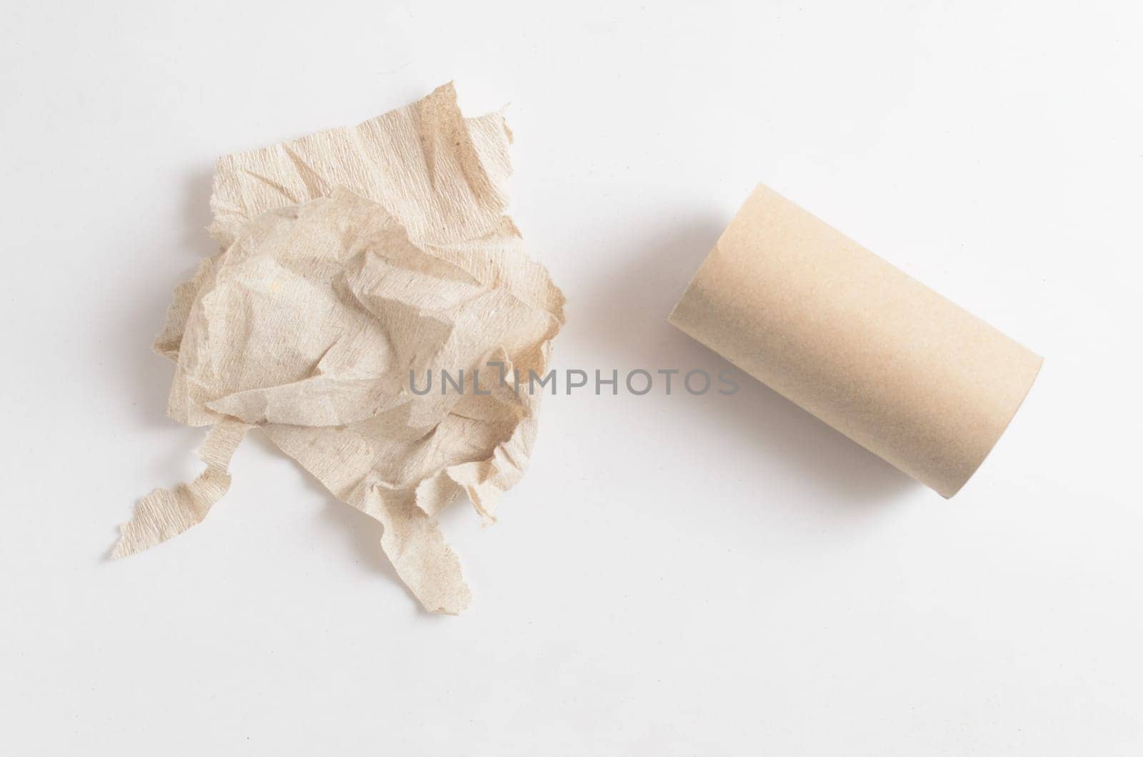 Crumpled toilet paper and empty toilet paper roll on white background.