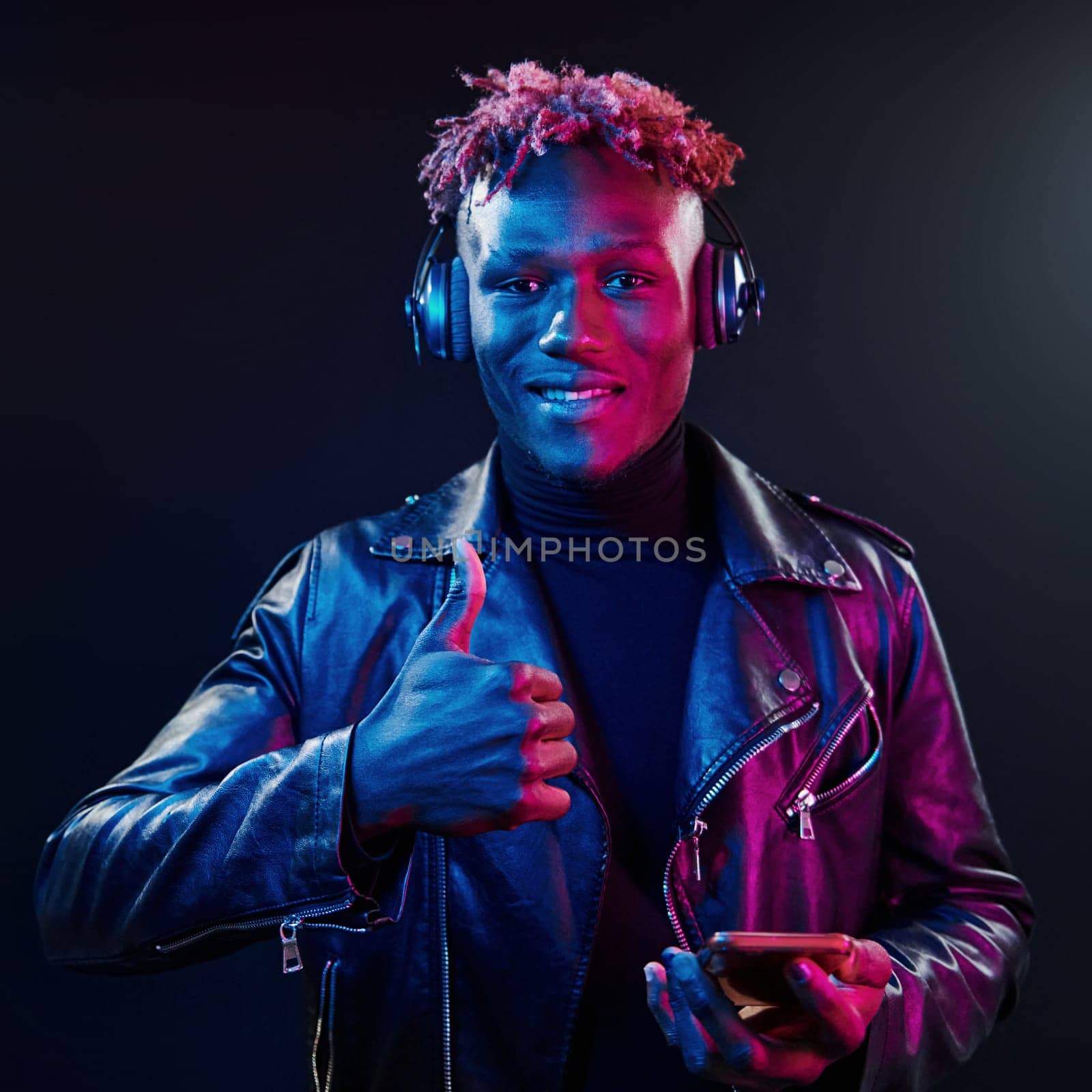 Dancing with headphones on. Futuristic neon lighting. Young african american man in the studio.