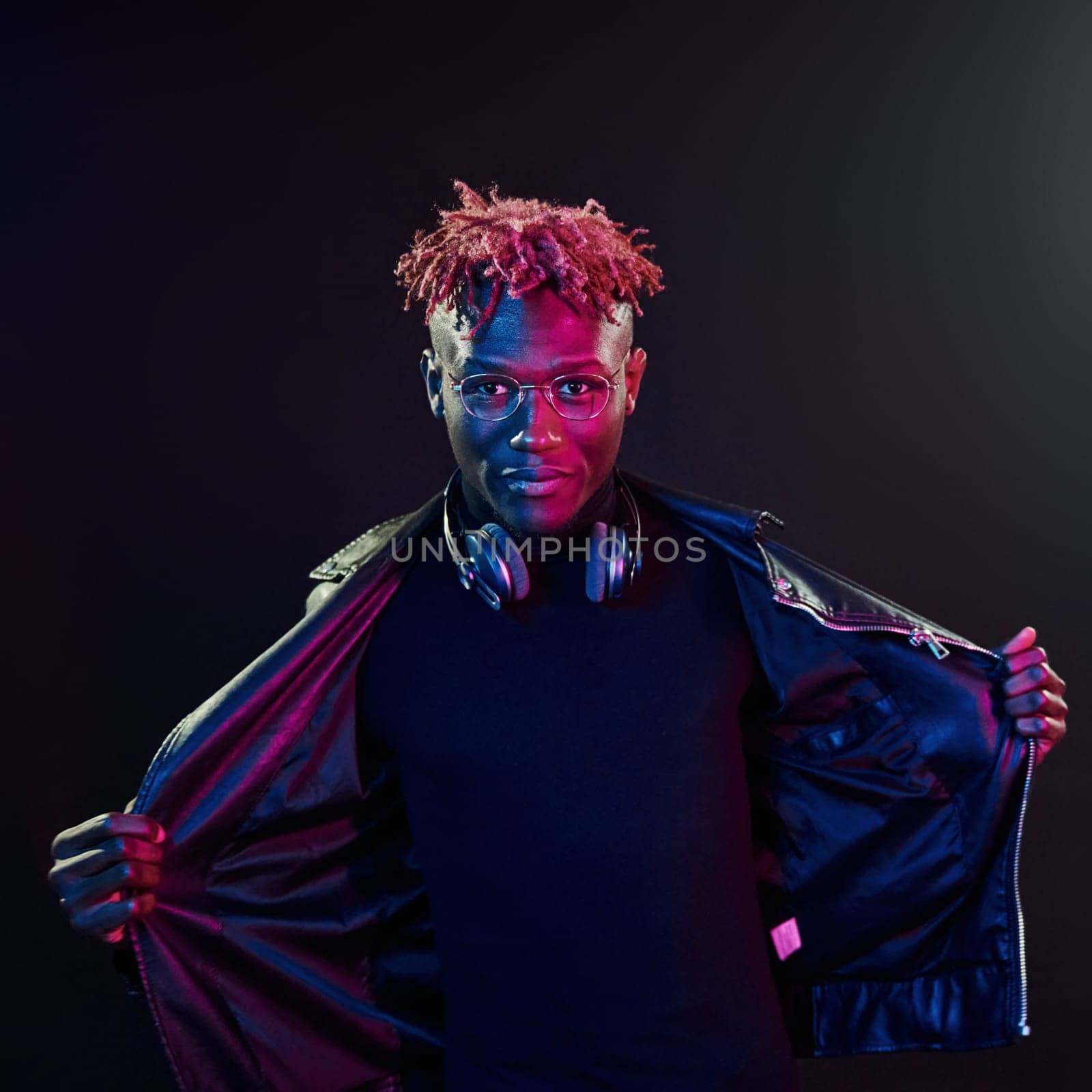 Posing with wireless headphones on neck. Futuristic neon lighting. Young african american man in the studio.