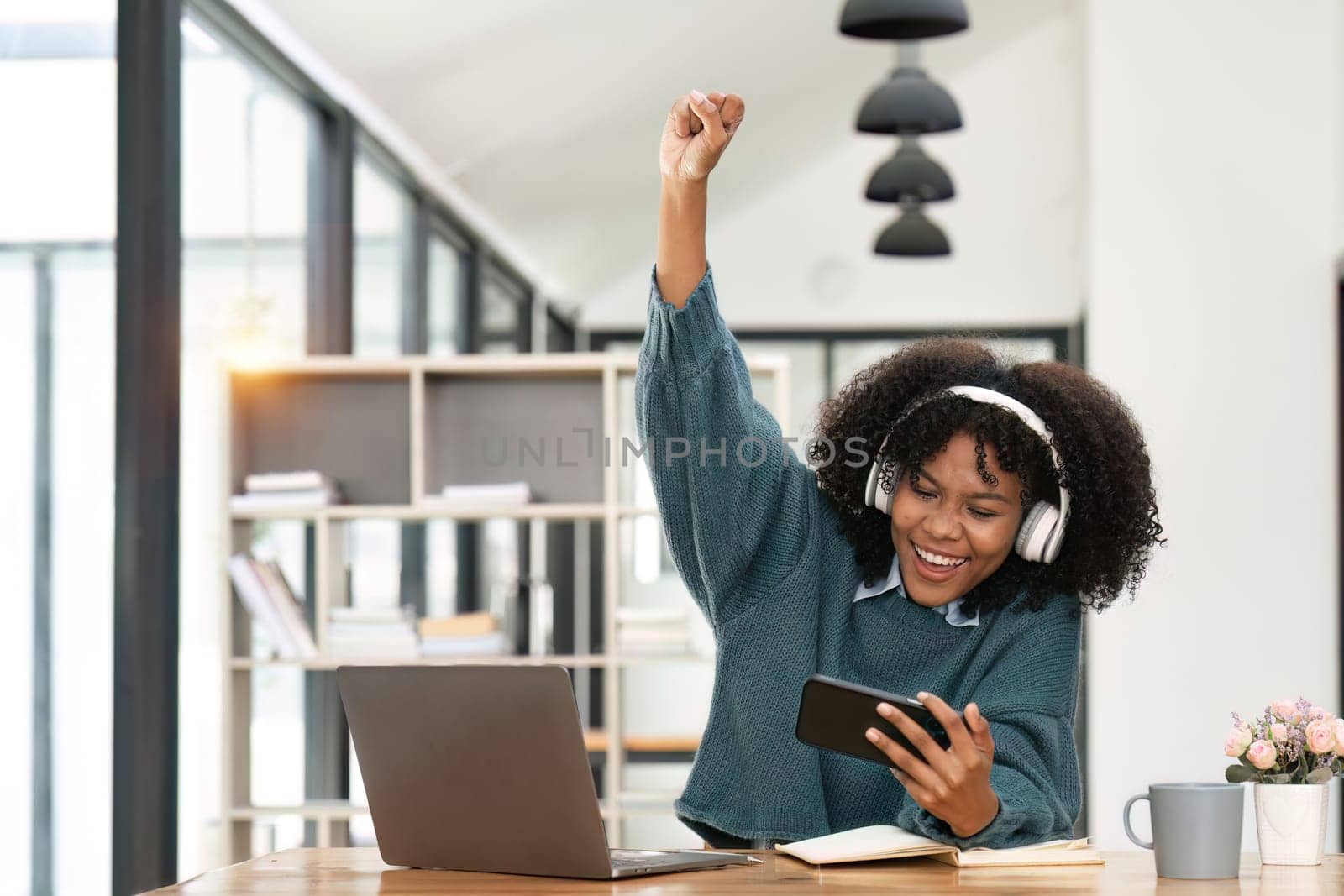 Excited african american in headphone hold smartphone feel euphoric reading good news, overjoyed happy black biracial young woman use cellphone triumph win online gaming by nateemee