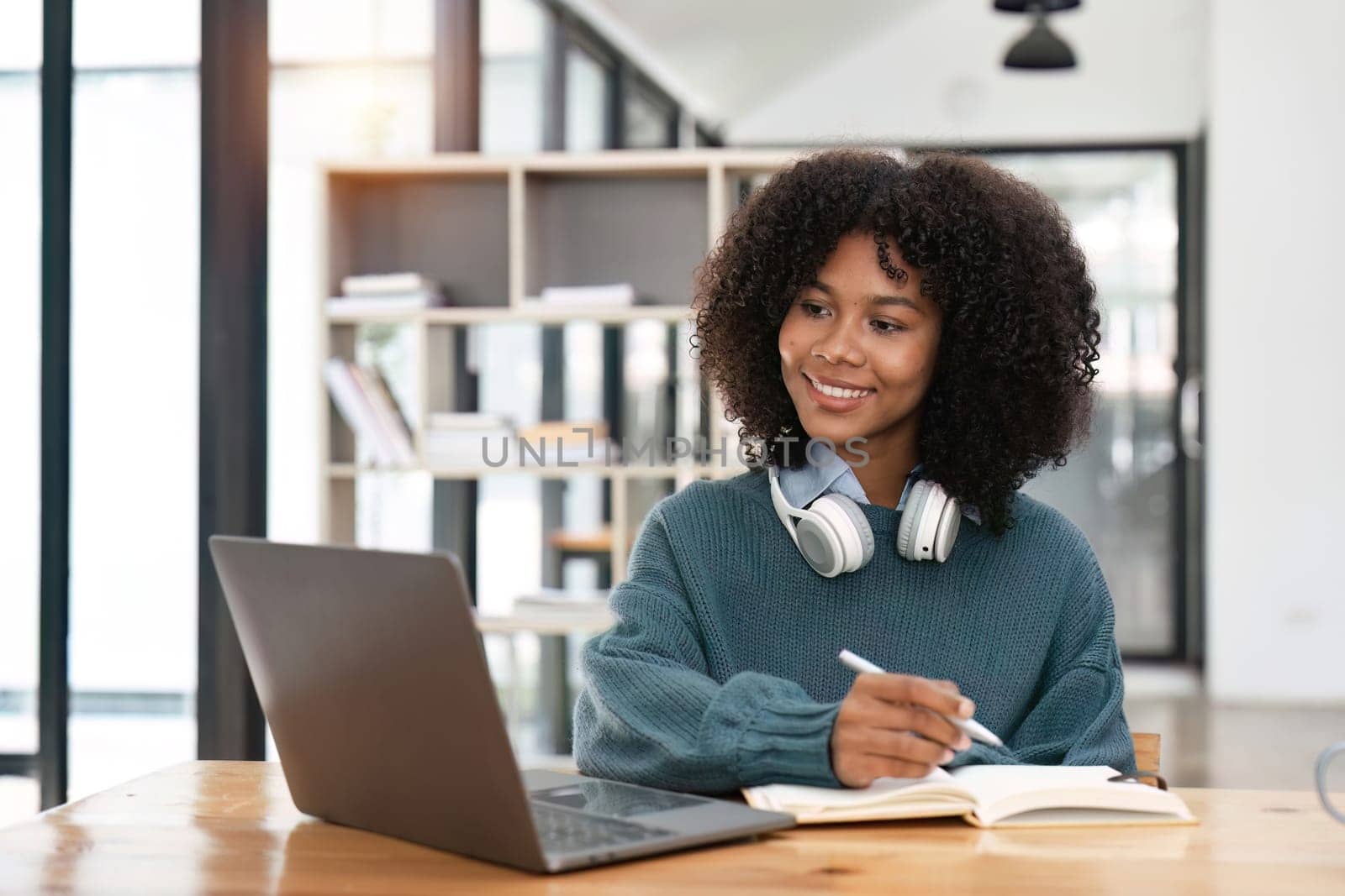 Smiling young african american teen girl wear headphones video calling on laptop. Happy woman student looking at computer screen watching webinar or doing video chat by webcam..