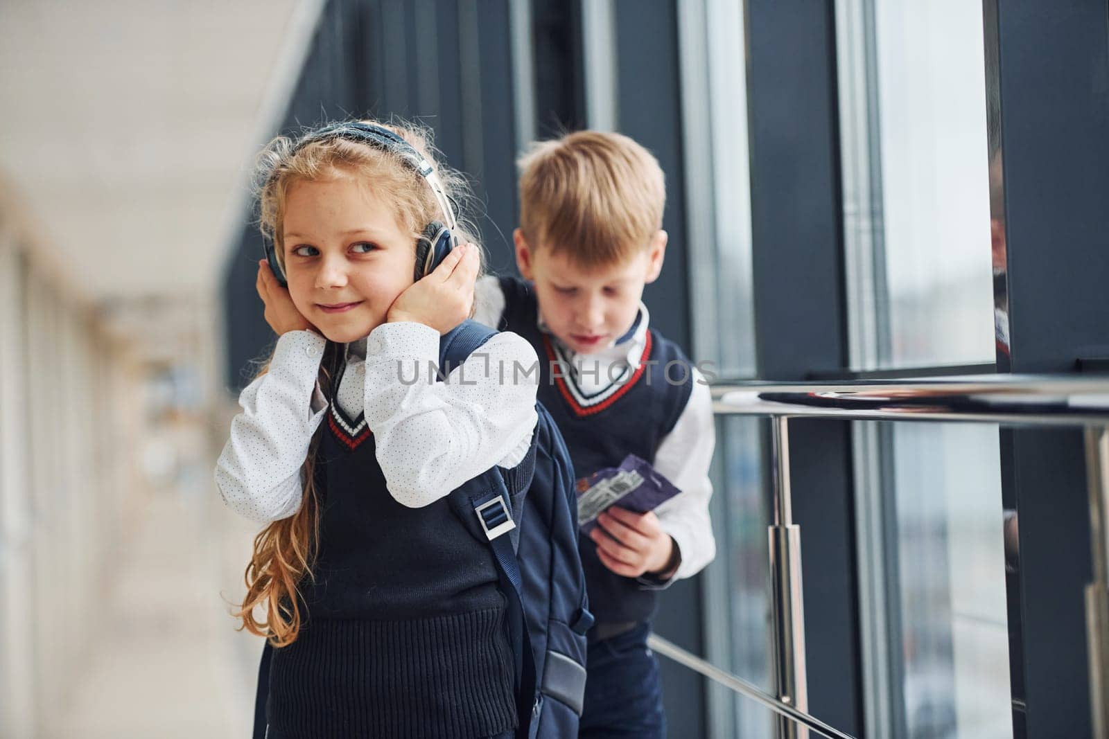 Little girl with headphones in uniform that together with boy in corridor. Conception of education by Standret