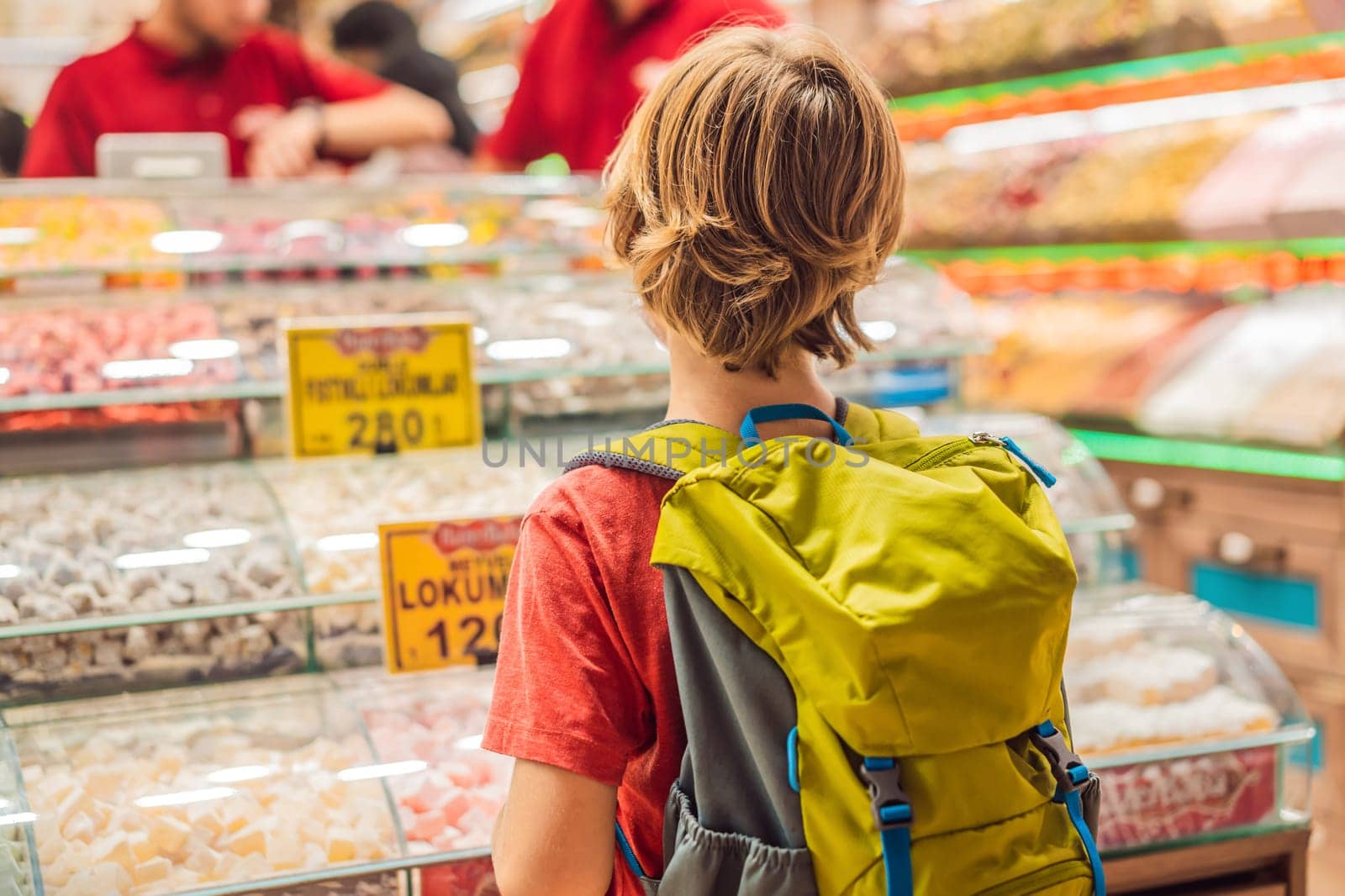The boy looks at the counter with Turkish sweets. Traditional oriental sweet pastry cookies, nuts, dried fruits, pastilles, marmalade, Turkish desert with sugar, honey and pistachio, in display at a street food market.