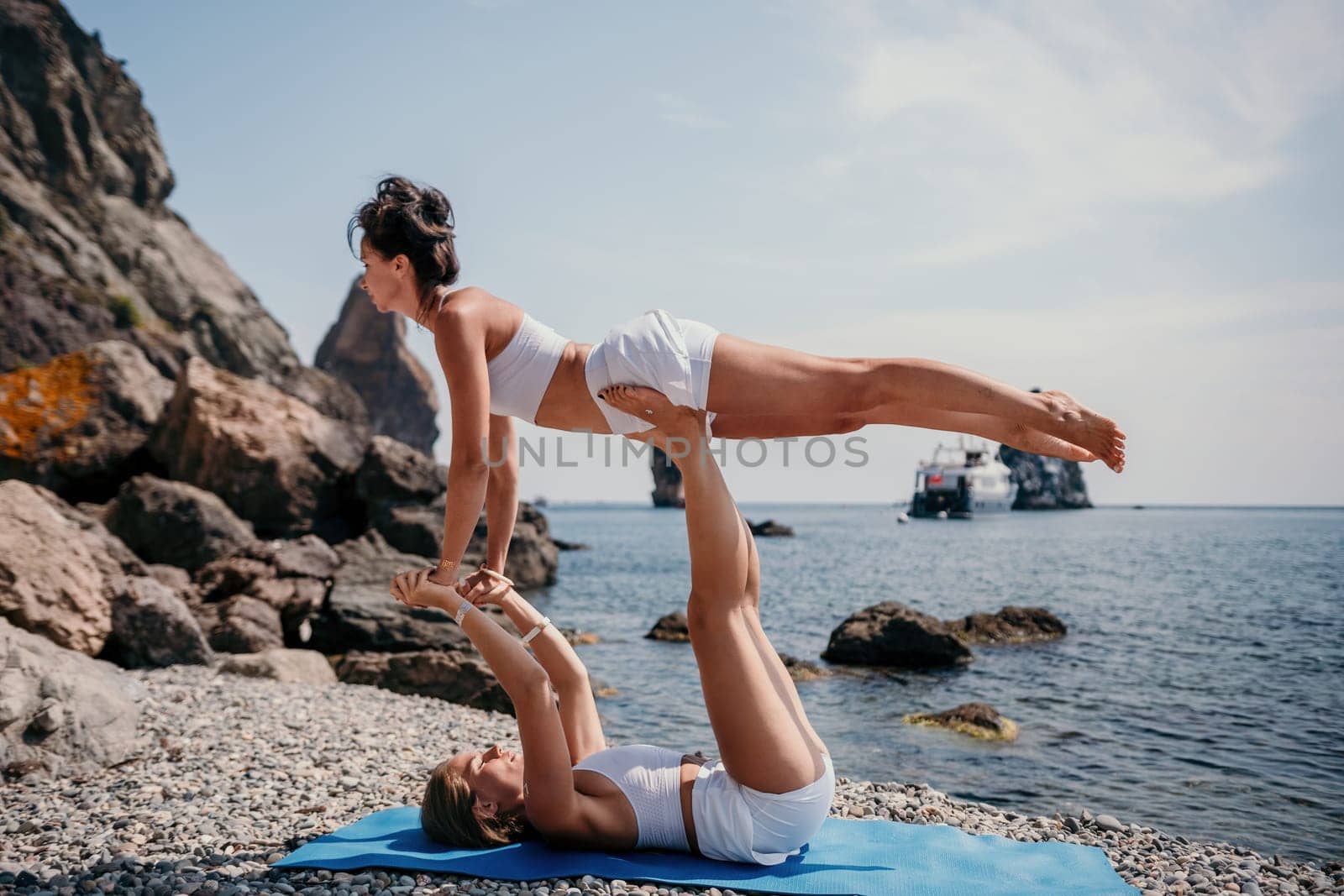 Woman sea yoga. Two Happy women meditating in yoga pose on the beach, ocean and rock mountains. Motivation and inspirational fit and exercising. Healthy lifestyle outdoors in nature, fitness concept. by panophotograph