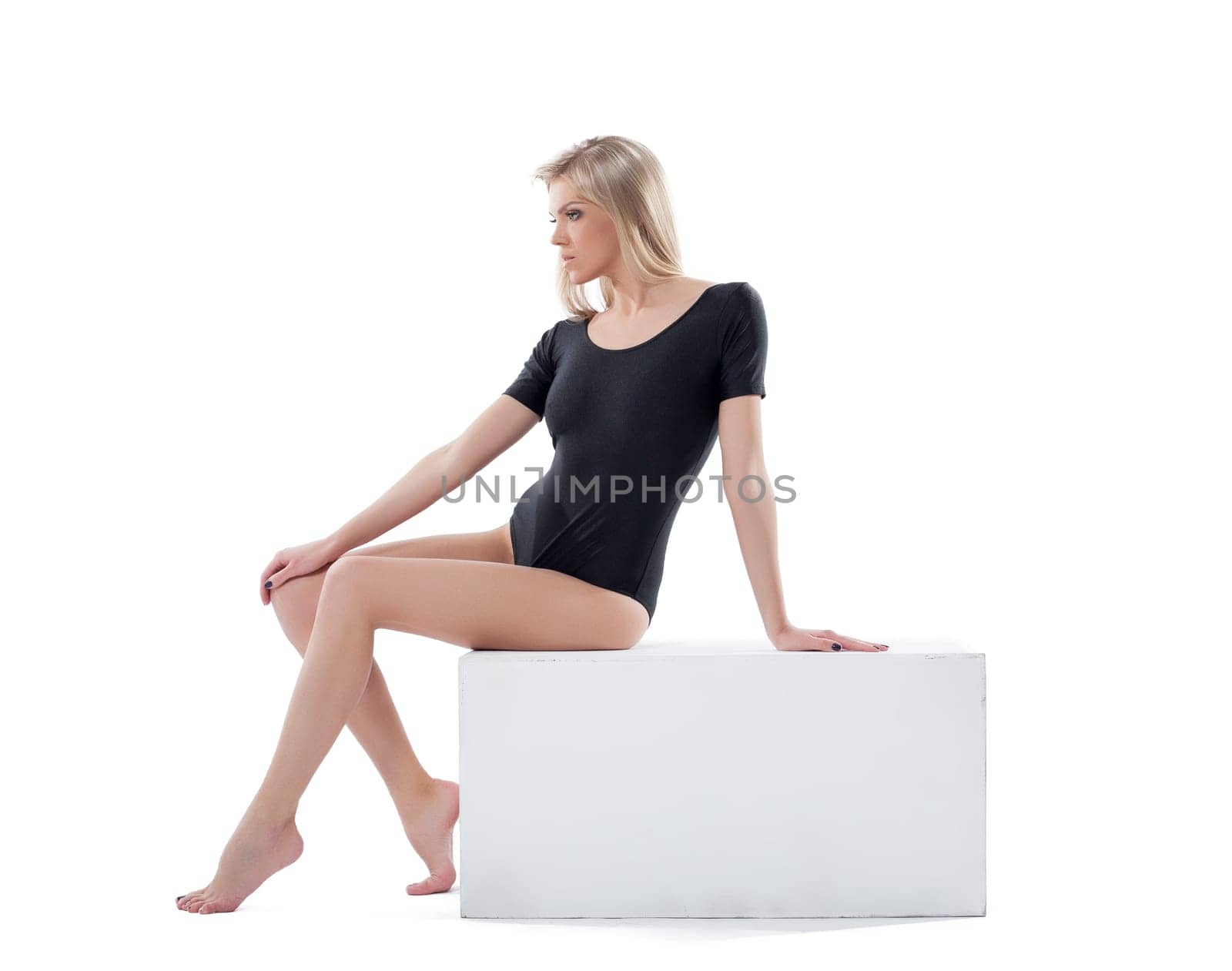 Sensual young blonde posing sitting on cube, isolated over white background