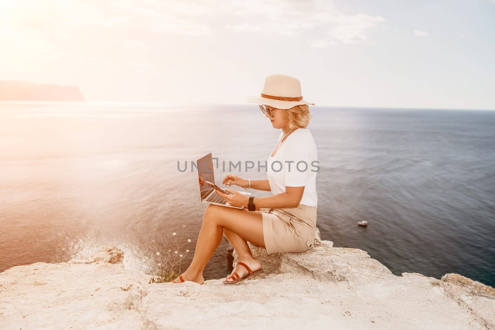 Digital nomad, Business woman working on laptop by the sea. Pretty lady typing on computer by the sea at sunset, makes a business transaction online from a distance. Freelance, remote work on vacation by panophotograph