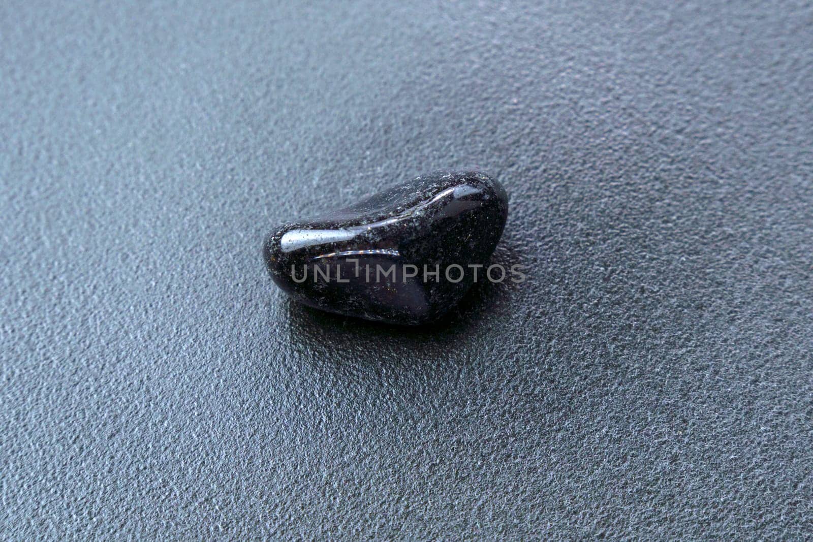Close up of natural mineral from geological collection tumbled black onyx gem stone, black background