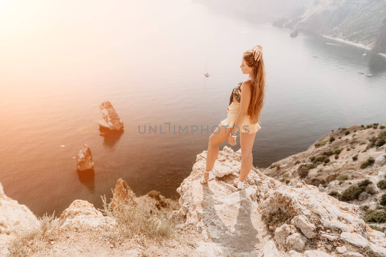 Woman travel sea. Happy tourist enjoy taking picture outdoors for memories. Woman traveler looks at the edge of the cliff on the sea bay of mountains, sharing travel adventure journey by panophotograph