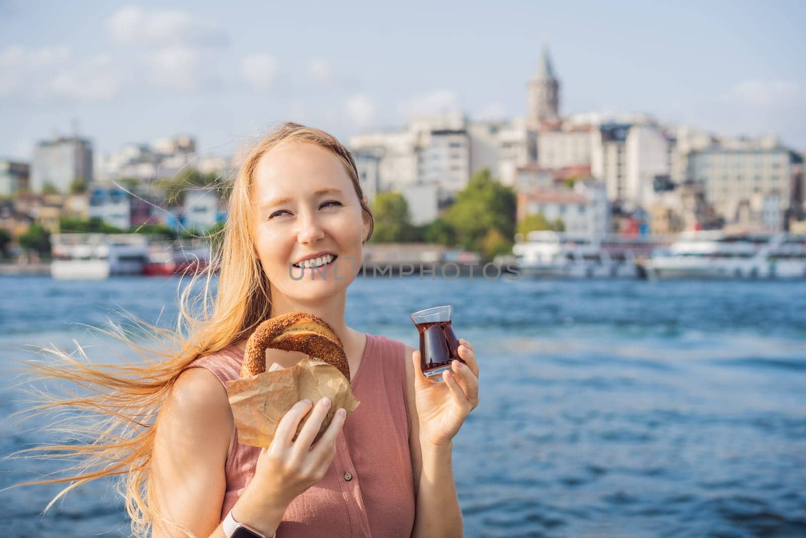 Woman in Istanbul having breakfast with Simit and a glass of Turkish tea. Glass of Turkish tea and bagel Simit against golden horn bay and the Galata Tower in Istanbul, Turkey. Turkiye by galitskaya