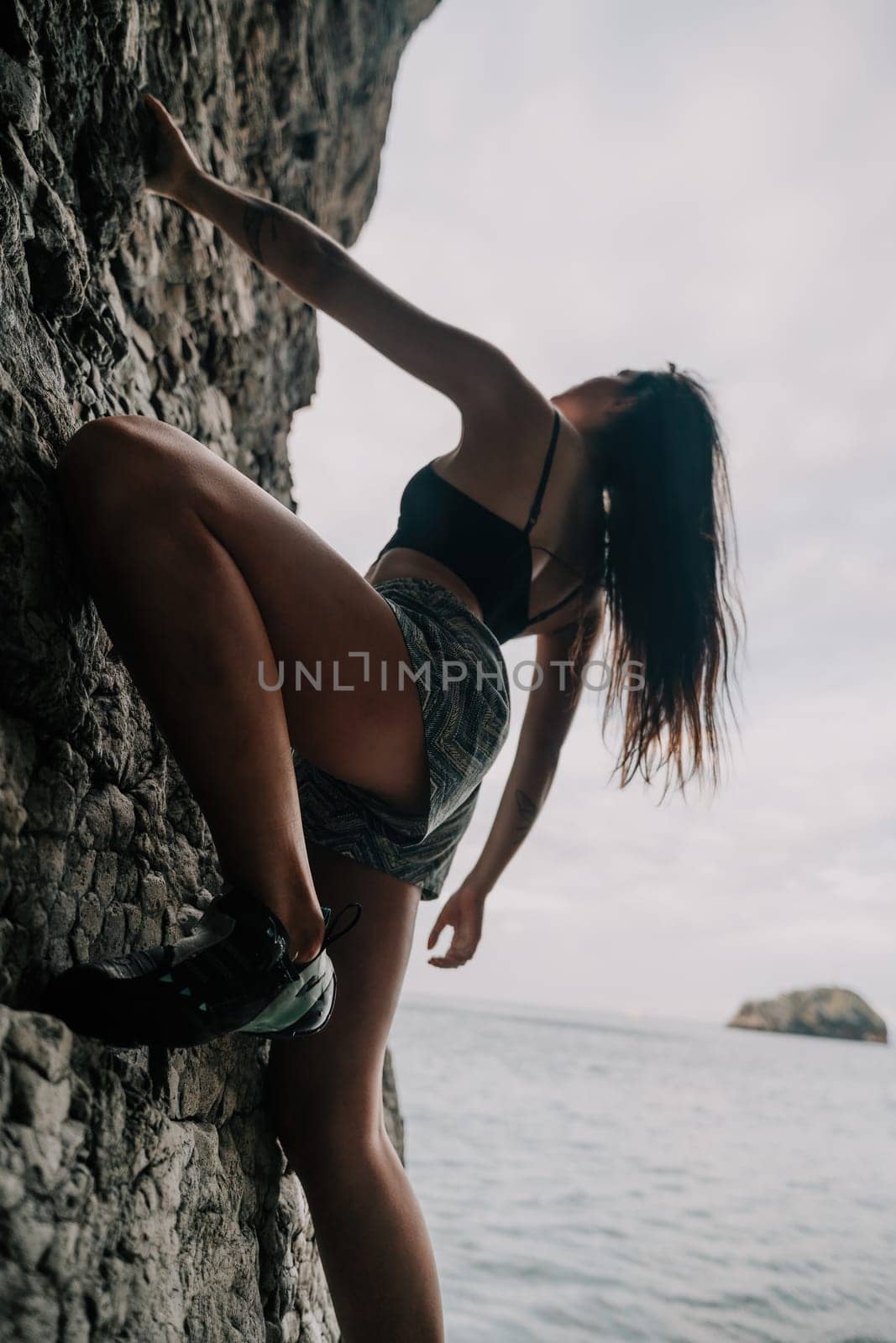 A girl climbs a rock. The athlete trains in nature. Woman overcomes difficult climbing route. Extreme hobby. Tourist woman rock climber hiking on mountains rocks over beautiful sea coast