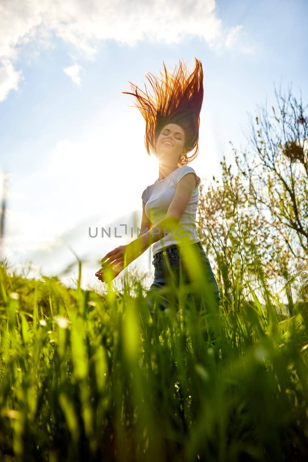 a happy woman in summer clothes stands in a field lit from behind and with her hair flying in the air. High quality photo