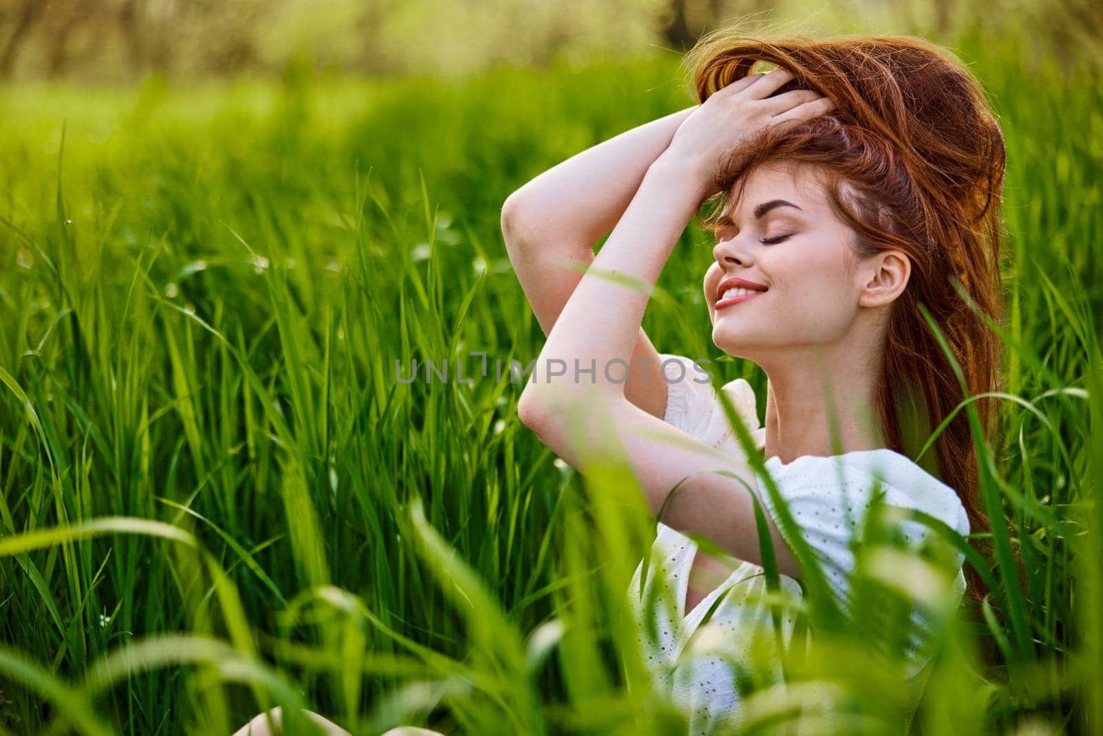 portrait of a beautiful woman sitting in tall grass and holding her long hair by Vichizh