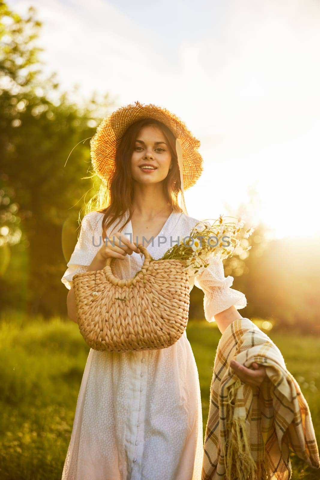 portrait of a happily smiling woman in a field lit from the back by the rays of the setting sun with a basket of flowers and a blanket in her hands by Vichizh