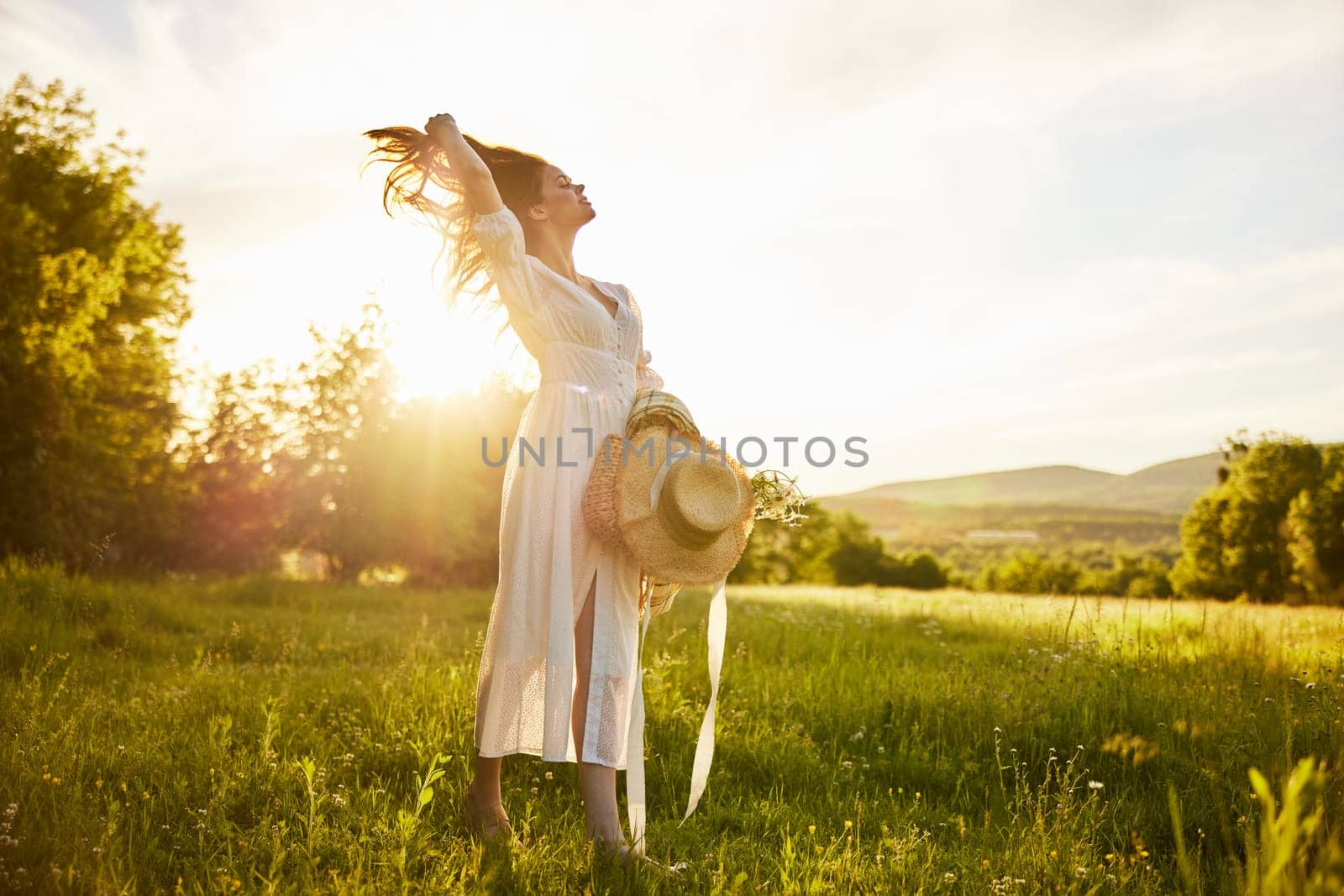 horizontal photo of a woman in a long light dress walking through the forest, illuminated from the back by the rays of the setting sun and straightening her hair. High quality photo