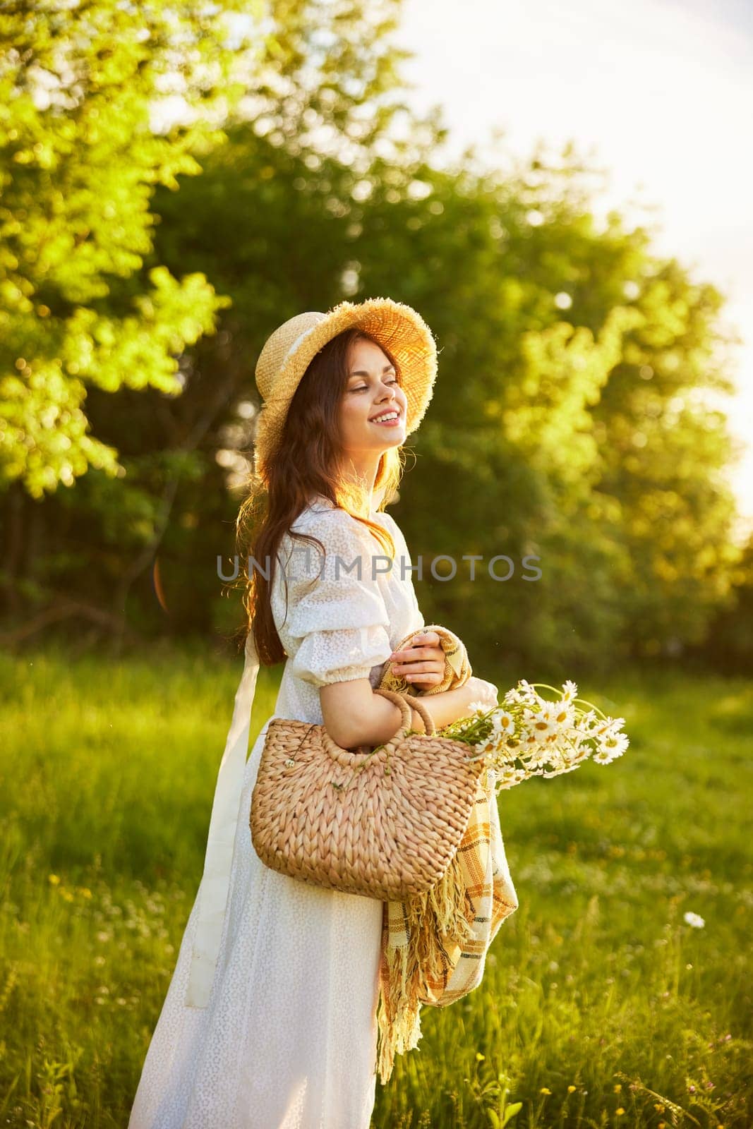 portrait of a happily smiling woman in a field lit from the back by the rays of the setting sun with a basket of flowers and a blanket in her hands by Vichizh