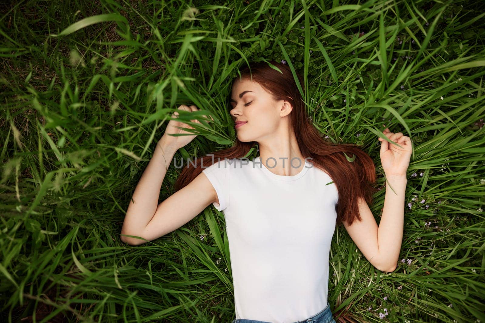 woman resting in nature with long red hair lies in green grass. High quality photo