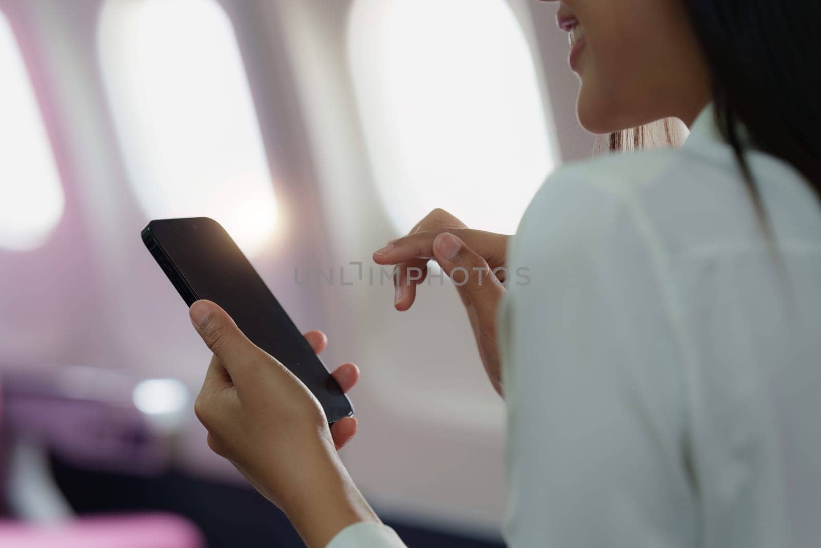 Beautiful Asian business woman chatting with client by mobile phone during flight. working, travel, business concept.