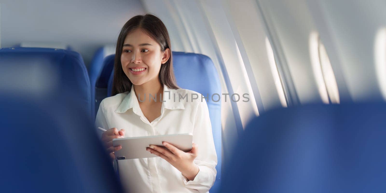 Beautiful Asian businesswoman working with digital tablet in aeroplane. working, travel, business concept by itchaznong