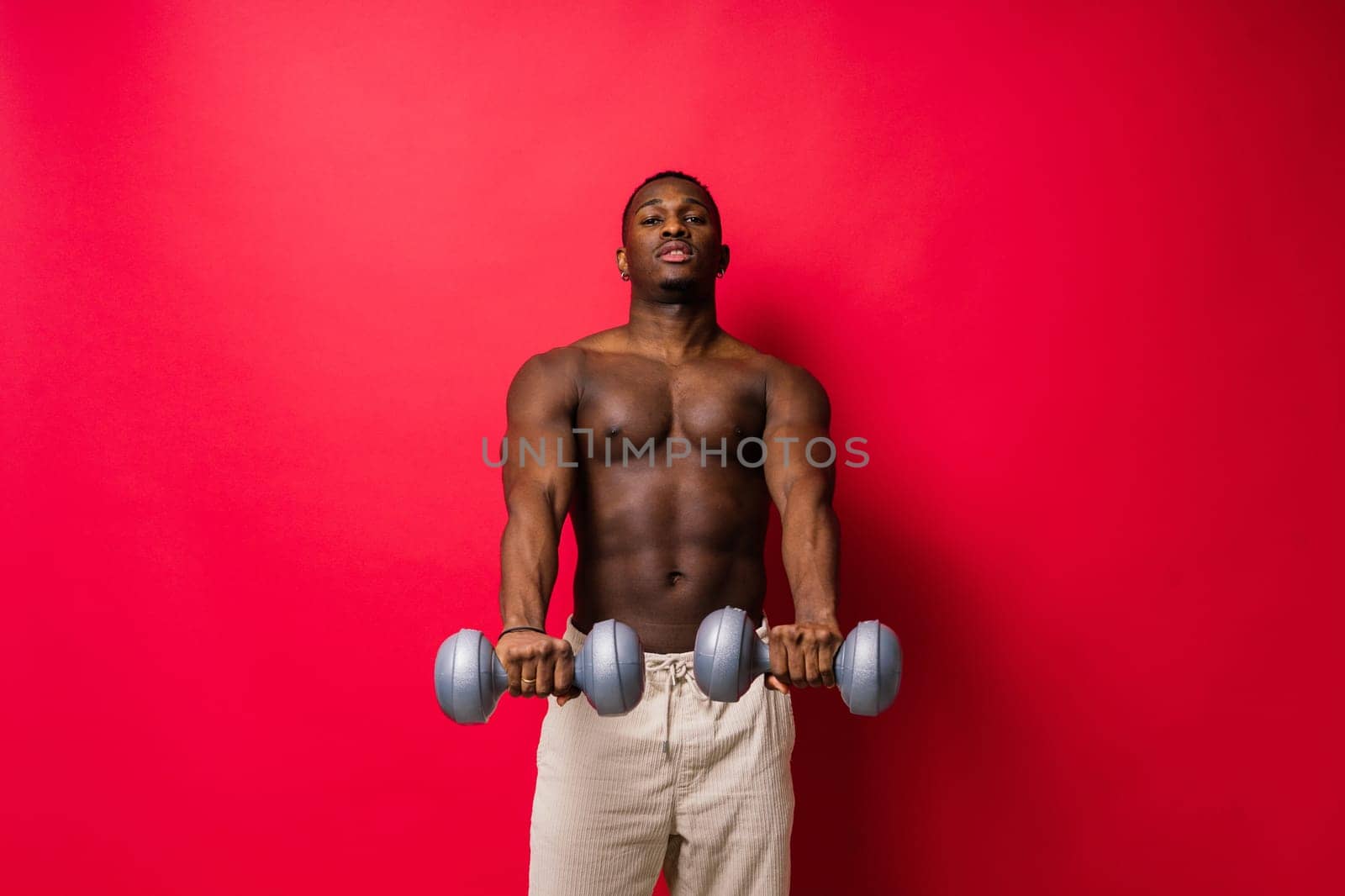 Portrait of a happy african man with dumbbells over red and black background by Zelenin