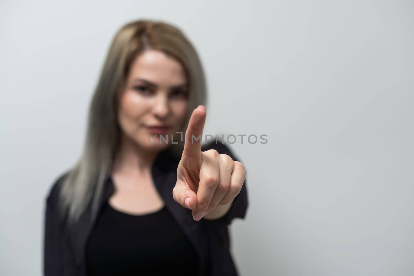 Studio shot of a young blond woman pointing towards you.