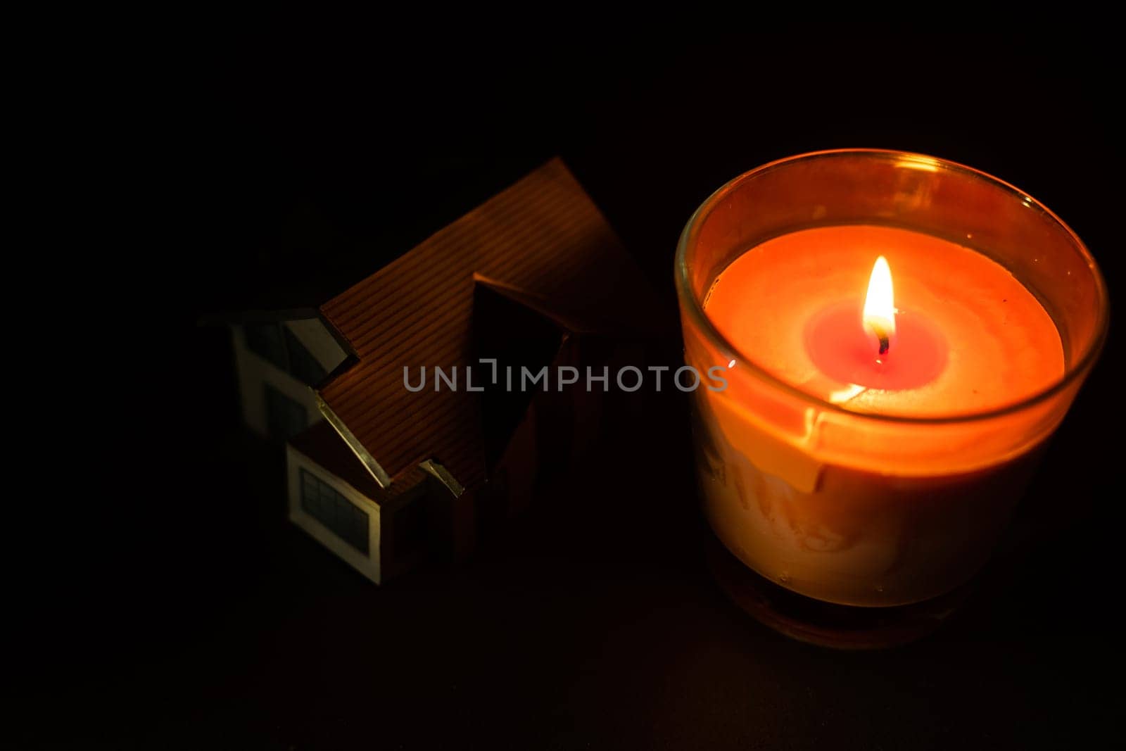 a candle and a toy house on dark background.