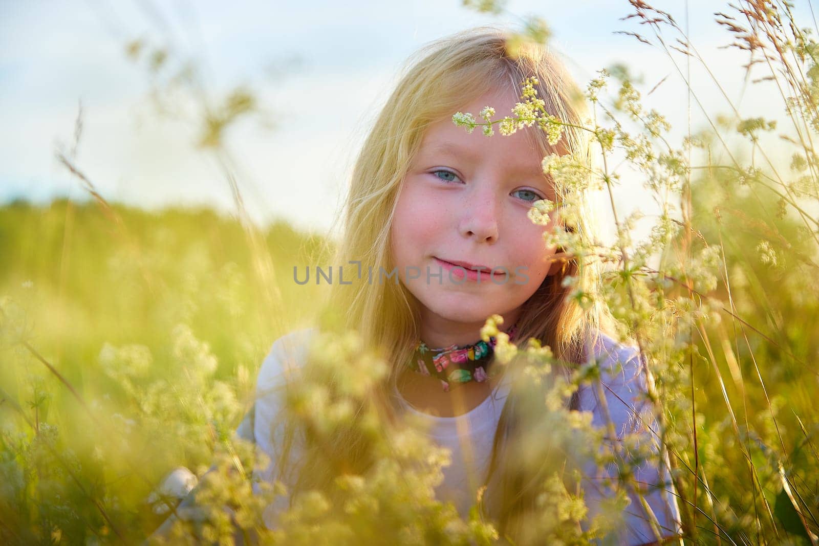 Portrait of pretty blonde girl having fun in a meadow on a natural landscape with grass and flowers on a sunny summer day. Portrait of a teenage child in summer or spring outdoors on field