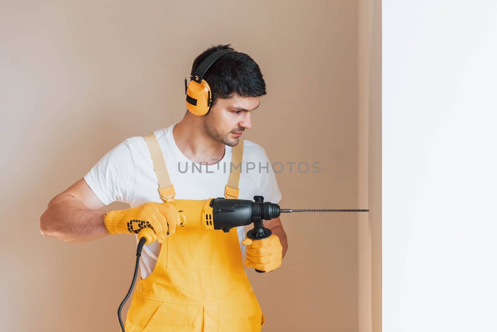 Handyman in yellow uniform works indoors by using hammer drill. House renovation conception.