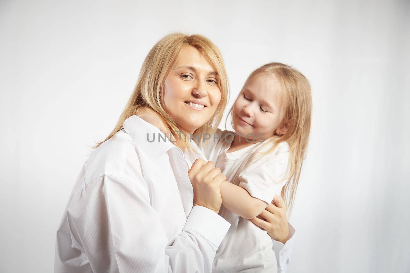 Portrait of blonde mother and daughter who having communicate and play on a white background. Mom and little girl models pose in the studio. The concept of love, friendship, caring in the family