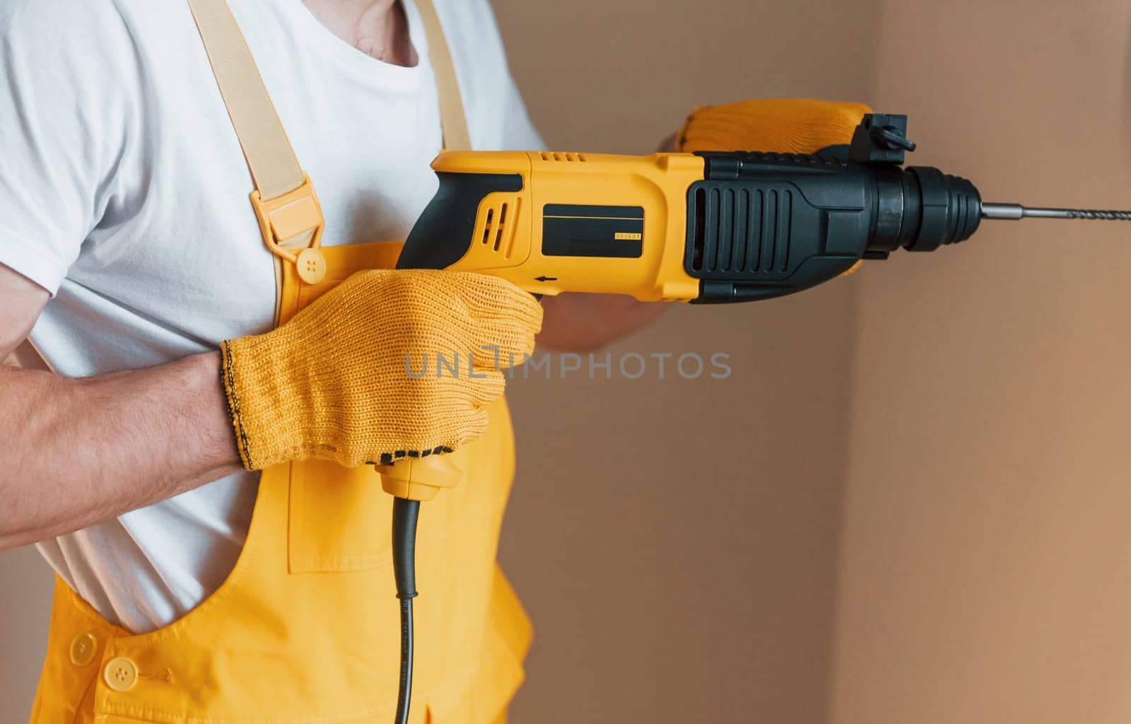 Handyman in yellow uniform works indoors by using hammer drill. House renovation conception.
