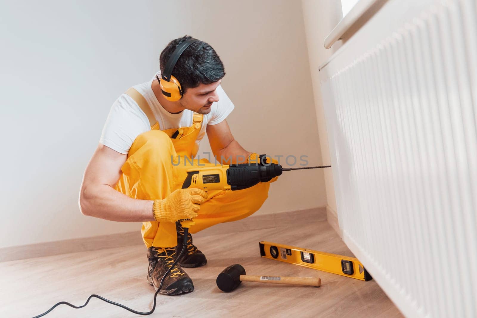 Handyman in yellow uniform works indoors by using hammer drill. House renovation conception.